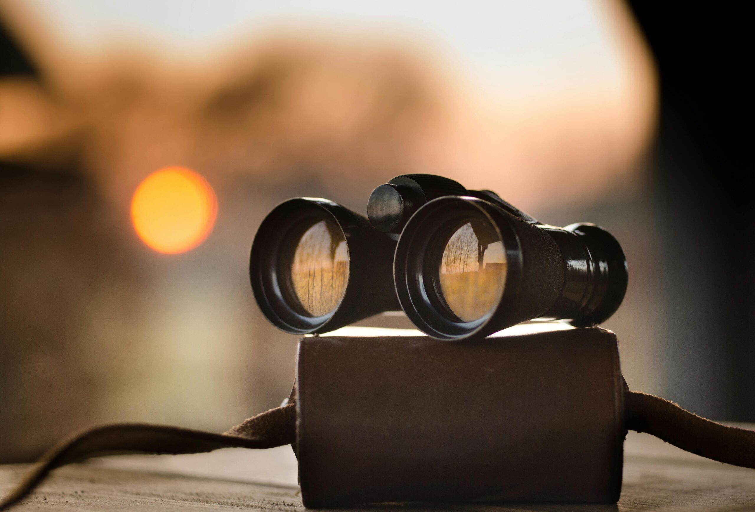 Close-up view of binoculars on a surface with sunset reflection in lenses.